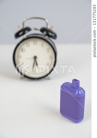 Disposable vape and alarm clock on white background.  131775283