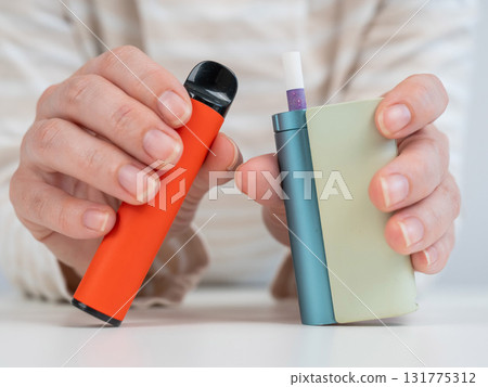 Woman holding electronic cigarette and disposable vape on white background. Tobacco heating systems and vaporizer.  131775312