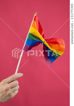Woman holding rainbow flag fastened with wedding ring on pink background. Woman holding rainbow flag fastened with wedding ring on pink background. 131775395