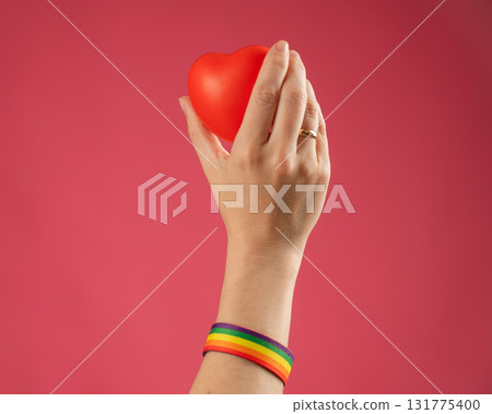 Woman with engagement ring and rainbow bracelet holding heart on pink background.  131775400