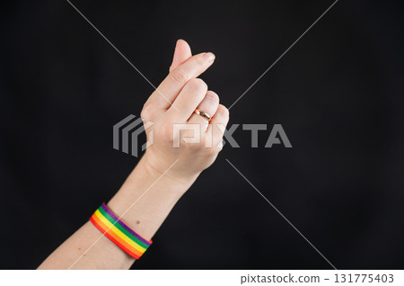 Woman with wedding ring and rainbow bracelet showing heart sign on black background.  Woman with wedding ring and rainbow bracelet showing heart sign on black background.  131775403