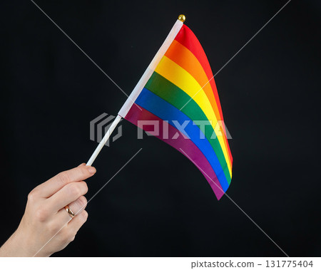 Woman with wedding ring holding rainbow flag on black background. Woman with wedding ring holding rainbow flag on black background. 131775404