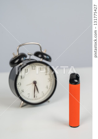 Disposable vape and alarm clock on white background. Disposable vape and alarm clock on white background. 131775427