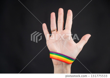 Woman with wedding ring and rainbow bracelet holding palm on black background.  131775533