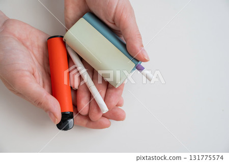 Woman holding regular, electronic cigarette and disposable vape on white background. Tobacco heating systems. 131775574