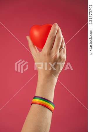 Woman with engagement ring and rainbow bracelet holding heart on pink background. Woman with engagement ring and rainbow bracelet holding heart on pink background. 131775741