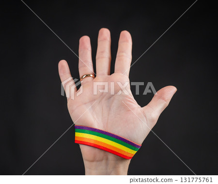 Woman with wedding ring and rainbow bracelet holding palm on black background. Woman with wedding ring and rainbow bracelet holding palm on black background. 131775761