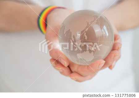 Woman wearing rainbow flag bracelet holding glass globe. Woman wearing rainbow flag bracelet holding glass globe. 131775806