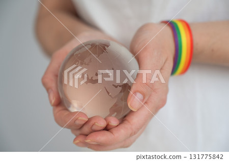 Woman wearing rainbow flag bracelet holding glass globe. Woman wearing rainbow flag bracelet holding glass globe. 131775842