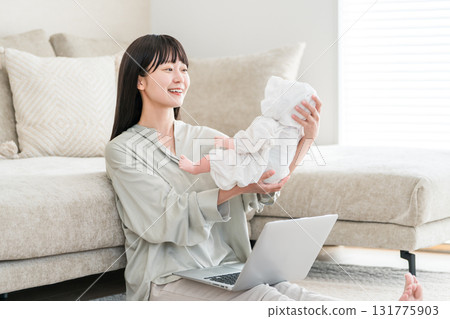 Young Asian woman looking at a laptop while holding a baby Young Asian woman looking at a laptop while holding a baby 131775903