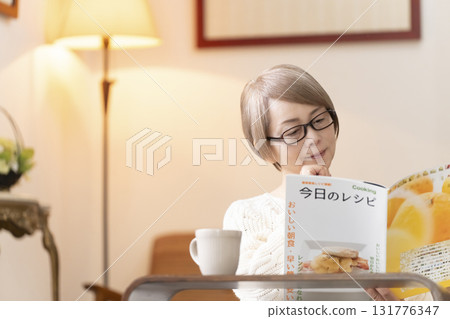 Senior woman looking at a recipe book in the living room 131776347