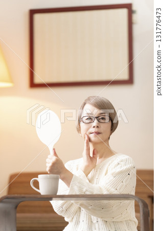Senior woman looking at a hand mirror in the living room Senior woman looking at a hand mirror in the living room 131776473