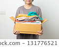 Donation Concept, woman holding clothes with donate box in white background room. 131776521