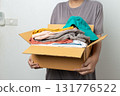 Donation Concept, woman holding clothes with donate box in white background room. 131776522