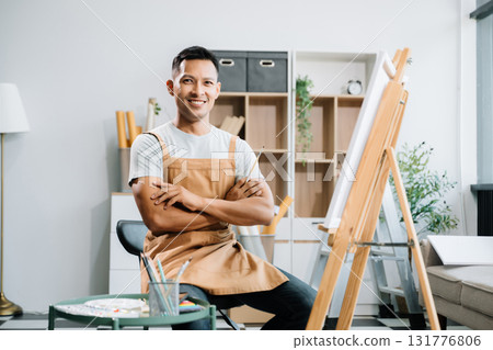 Asian male painter do artwork in art workshop, painting supplies, oil pastels, two canvas easel, creative space with paintbrush in art studio 131776806