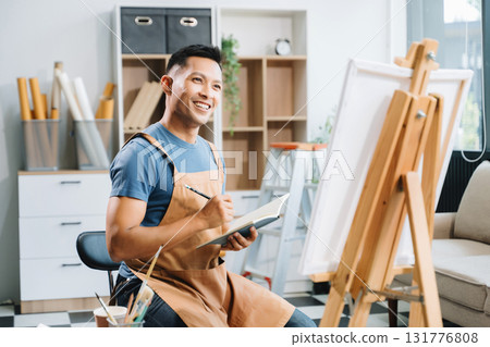 Asian male painter do artwork in art workshop, painting supplies, oil pastels, two canvas easel, creative space with paintbrush in art studio Asian male painter do artwork in art workshop, painting supplies, oil pastels, two canvas easel, creative space with paintbrush in art studio 131776808