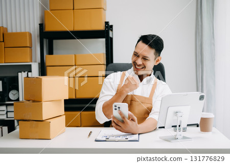 Startup small business SME, Entrepreneur owner man using smartphone or tablet taking receive and checking online purchase shopping order to preparing pack product box. in office Startup small business SME, Entrepreneur owner man using smartphone or tablet taking receive and checking online purchase shopping order to preparing pack product box. in office 131776829