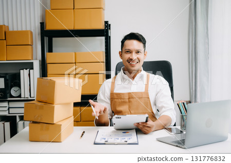 Startup small business SME, Entrepreneur owner man using smartphone or tablet taking receive and checking online purchase shopping order to preparing pack product box. in office Startup small business SME, Entrepreneur owner man using smartphone or tablet taking receive and checking online purchase shopping order to preparing pack product box. in office 131776832