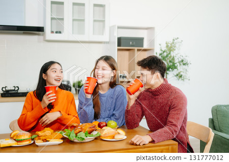 Young Asian friends enjoy a cozy dinner party at home, sharing food, drinks, and laughter in a warm modern kitchen. 131777012