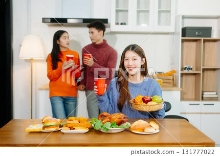 Young Asian friends enjoy a cozy dinner party at home, sharing food, drinks, and laughter in a warm modern kitchen. Young Asian friends enjoy a cozy dinner party at home, sharing food, drinks, and laughter in a warm modern kitchen. 131777022