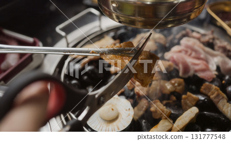 Hand cooking smoked grilled pork on iron grill pan in Korean BBQ in restaurant. Traditional Korea style food barbecue pork belly steak on charcoal grill. Hand cooking smoked grilled pork on iron grill pan in Korean BBQ in restaurant. Traditional Korea style food barbecue pork belly steak on charcoal grill. 131777548