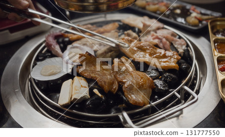 Hand cooking smoked grilled pork on iron grill pan in Korean BBQ in restaurant. Traditional Korea style food barbecue pork belly steak on charcoal grill. 131777550