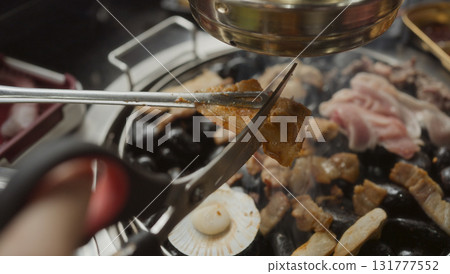 Hand cooking smoked grilled pork on iron grill pan in Korean BBQ in restaurant. Traditional Korea style food barbecue pork belly steak on charcoal grill. Hand cooking smoked grilled pork on iron grill pan in Korean BBQ in restaurant. Traditional Korea style food barbecue pork belly steak on charcoal grill. 131777552