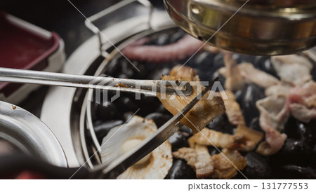 Hand cooking smoked grilled pork on iron grill pan in Korean BBQ in restaurant. Traditional Korea style food barbecue pork belly steak on charcoal grill. 131777553