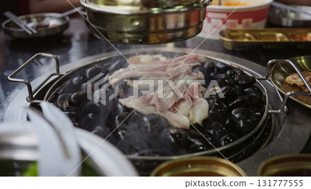 Hand cooking smoked grilled pork on iron grill pan in Korean BBQ in restaurant. Traditional Korea style food barbecue pork belly steak on charcoal grill. 131777555