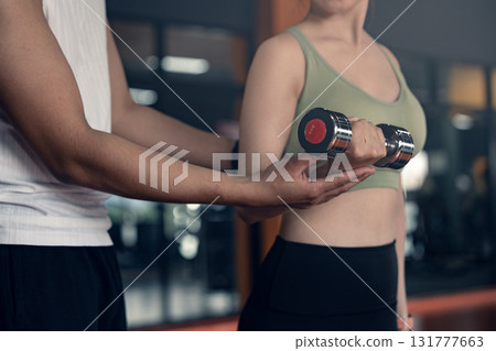 Young asian woman doing exercises with dumbbells in a gym while her trainer is supporting her. Young asian woman doing exercises with dumbbells in a gym while her trainer is supporting her. 131777663