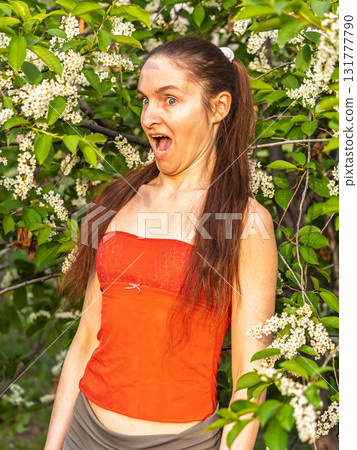 Young woman sneezes in the park against the background of a flowering tree. Allergy to pollen concept. Young woman sneezes in the park against the background of a flowering tree. Allergy to pollen concept. 131777790