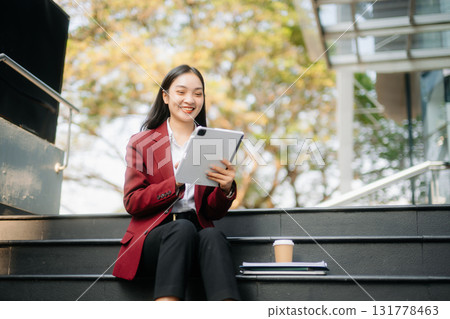 Confident Asian woman with a smile standing holding notepad and tablet at out side office. 131778463