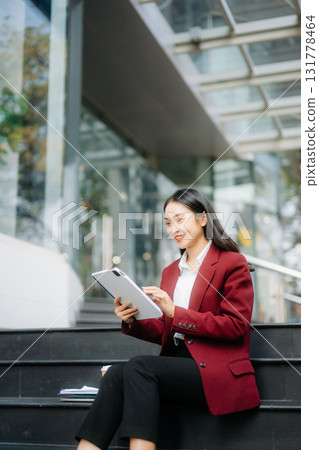 Confident Asian woman with a smile standing holding notepad and tablet at out side office. Confident Asian woman with a smile standing holding notepad and tablet at out side office. 131778464