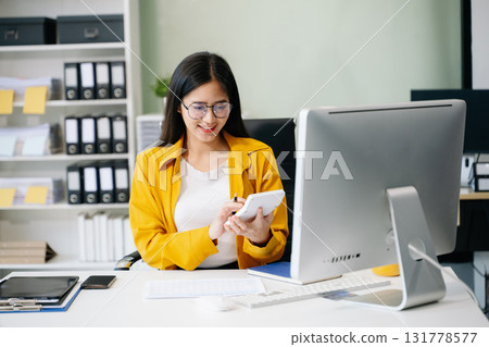 Young Asian businesswoman working with working notepad, tablet and laptop documents talking Young Asian businesswoman working with working notepad, tablet and laptop documents talking 131778577