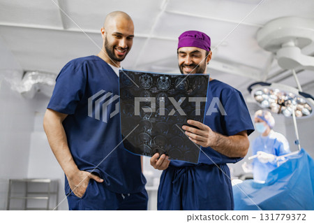 Two surgeons examine an X-ray in an operating room, with another medical professional in the background. Two surgeons examine an X-ray in an operating room, with another medical professional in the background. 131779372