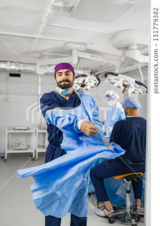 A surgeon is putting on a surgical gown in a modern operating room, preparing for a procedure with his team. A surgeon is putting on a surgical gown in a modern operating room, preparing for a procedure with his team. 131779382