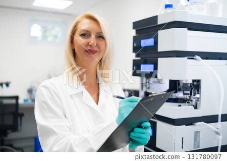Experienced woman researcher recording chromatography results during HPLC analysis in a modern lab. Concept of chemical testing and innovation. Experienced woman researcher recording chromatography results during HPLC analysis in a modern lab. Concept of chemical testing and innovation. 131780097