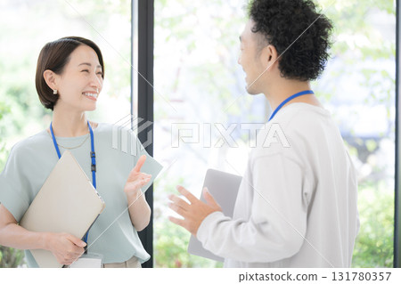 Smiling men and women wearing name tags talking by a window with greenery, holding computers, refreshing, talking office casual middle-aged business 131780357