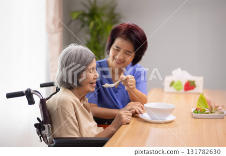 Caregiver feeding elderly asian woman with soup. 131782630