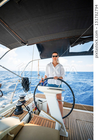 Young woman steering a sailing yacht near Croatia, confidently standing at the helm. Female leadership, empowerment and freedom in maritime lifestyle. 131782794