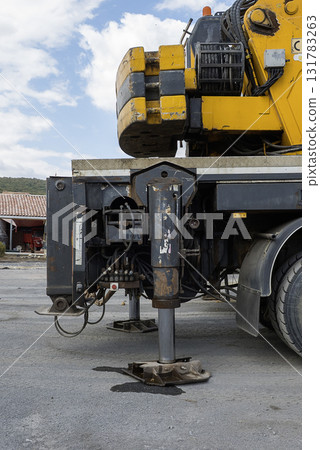 A large yellow and black Hidromek HMK 310 crane mounted on a flatbed truck is parked in a construction site. A large yellow and black Hidromek HMK 310 crane mounted on a flatbed truck is parked in a construction site. 131783263