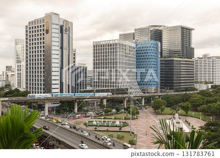 a prominent high-rise building, the BTS Skytrain on an elevated track, and roads with vehicular traffic below, all characteristic of a bustling city center like Bangkok. 131783761