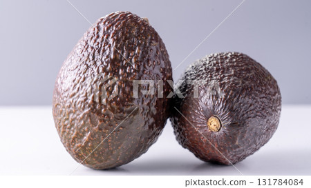Two fully ripened, unpeeled avocados, captured in close-up against a white backdrop. 131784084