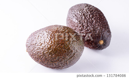 Two ripe, unpeeled avocados on a white background. 131784086