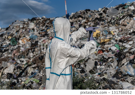 A worker in protective clothing inspects a landfill full of garbage, focusing on the impact of pollution and waste on the environment 131786052