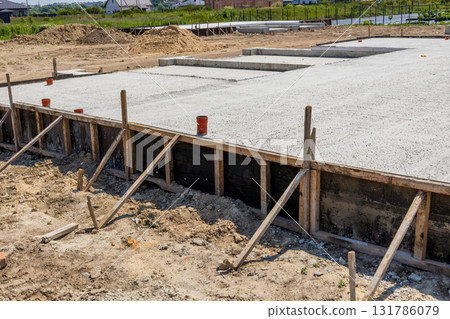 Construction workers pour cement to create a solid foundation for new houses on a development site under clear blue skies Construction workers pour cement to create a solid foundation for new houses on a development site under clear blue skies 131786079