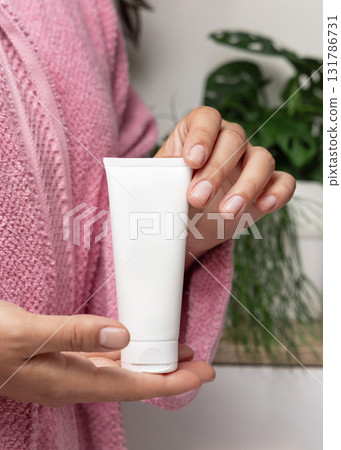 Closeup of woman in pink bathrobe holding white cream tube in hands, cosmetic mockup Closeup of woman in pink bathrobe holding white cream tube in hands, cosmetic mockup 131786731