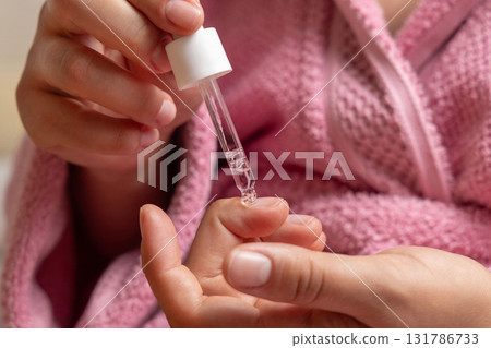 Woman in pink bathrobe dropping essential oil on a finger nail and holding a pipette closeup Woman in pink bathrobe dropping essential oil on a finger nail and holding a pipette closeup 131786733