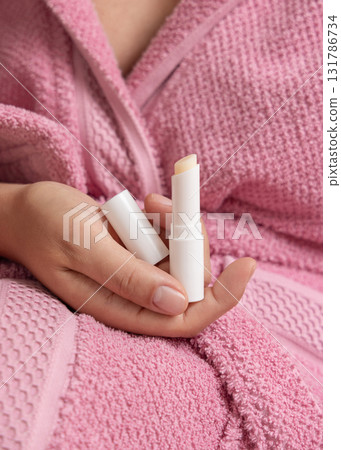 Woman in pink bathrobe holding in hand opened lip balm stick with a lid closeup, girly mockup Woman in pink bathrobe holding in hand opened lip balm stick with a lid closeup, girly mockup 131786734
