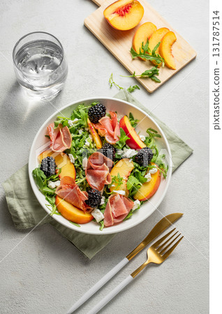 Fresh salad with peaches, arugula, feta, prosciutto and berries in a plate on a light background 131787514